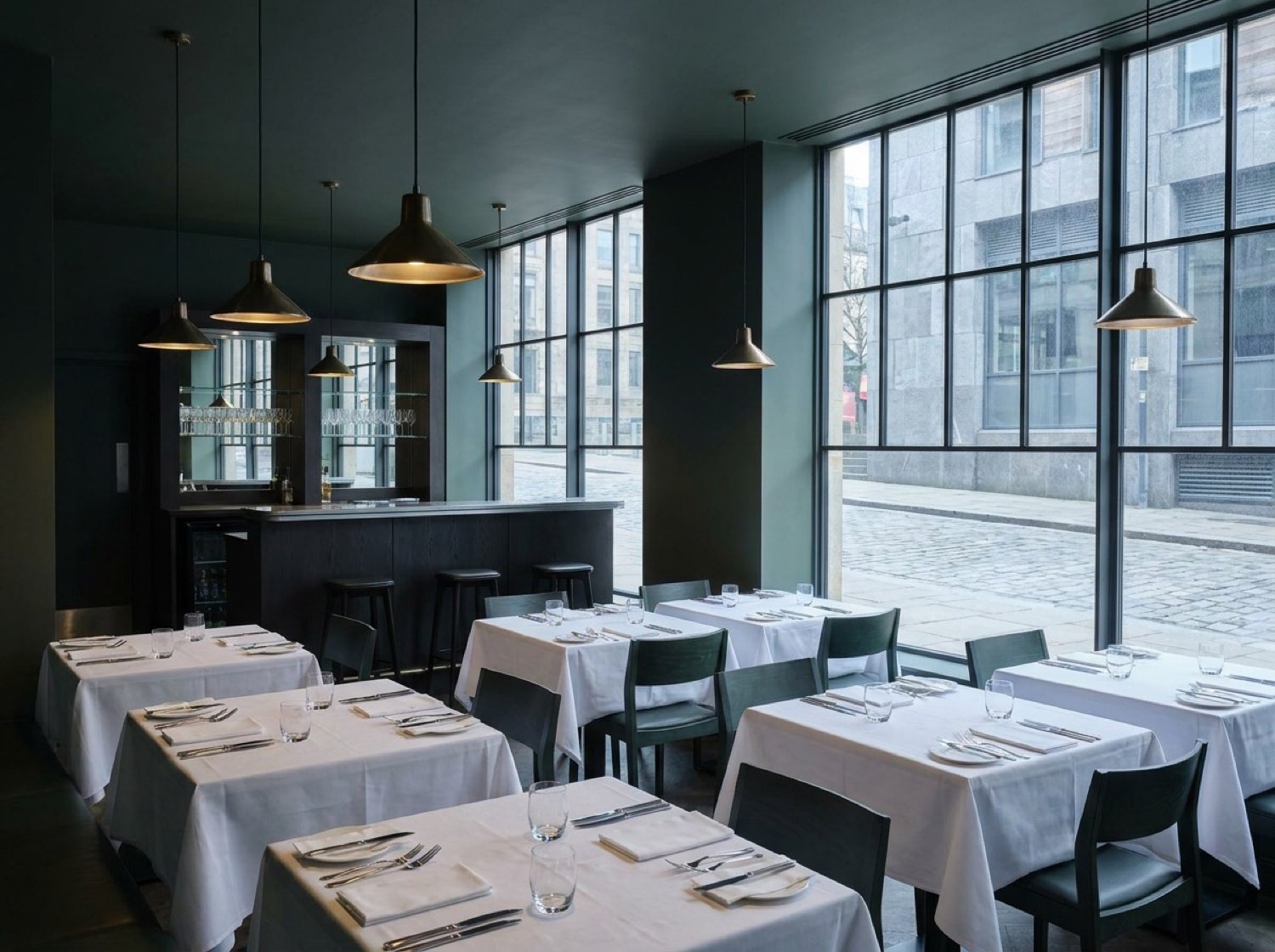PartyQueueCrew restaurant — set tables, low pendant lighting, dark green palette